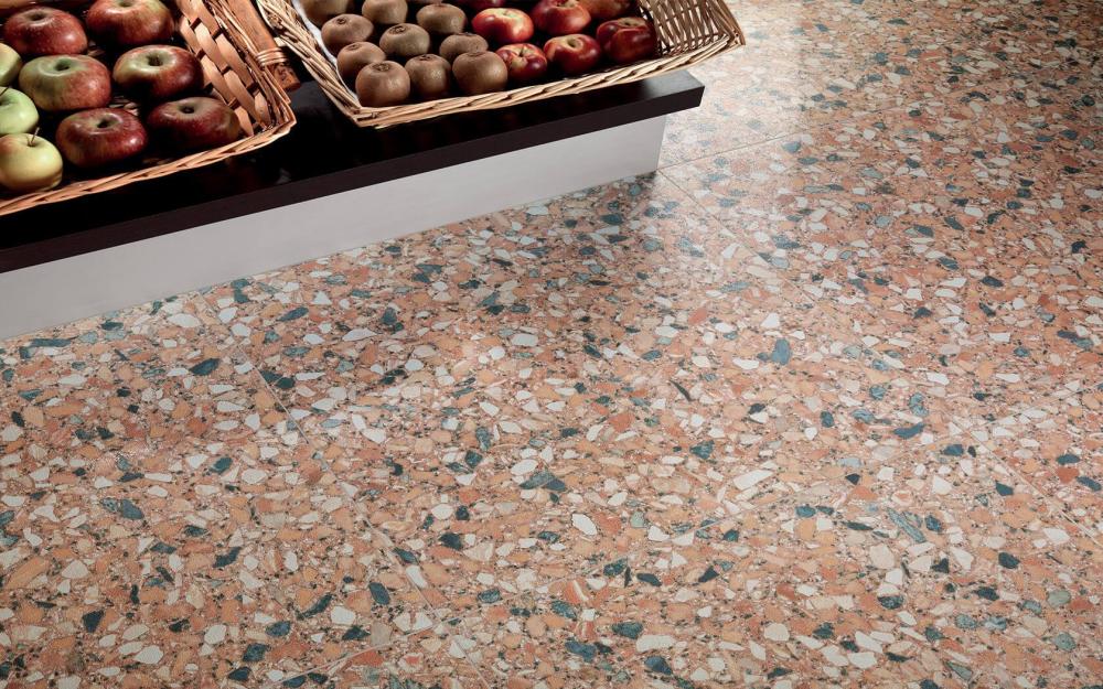 T&uuml;kilise mustriga terratso stiilis p&otilde;randaplaadid kaupluse puuviljaletis, millel on korvides &otilde;unad ja kiivid. Soe toon ja mitmev&auml;rviline killustik loovad loodusl&auml;hedase ja vastupidava p&otilde;randapinna.