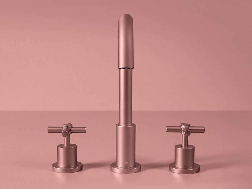 Kaasaegne kolmest osast koosnev vannitoa segisti siidise roosatooni viimistlusega, keskne tila ja kaks ristkäepidet, roosakal taustal.