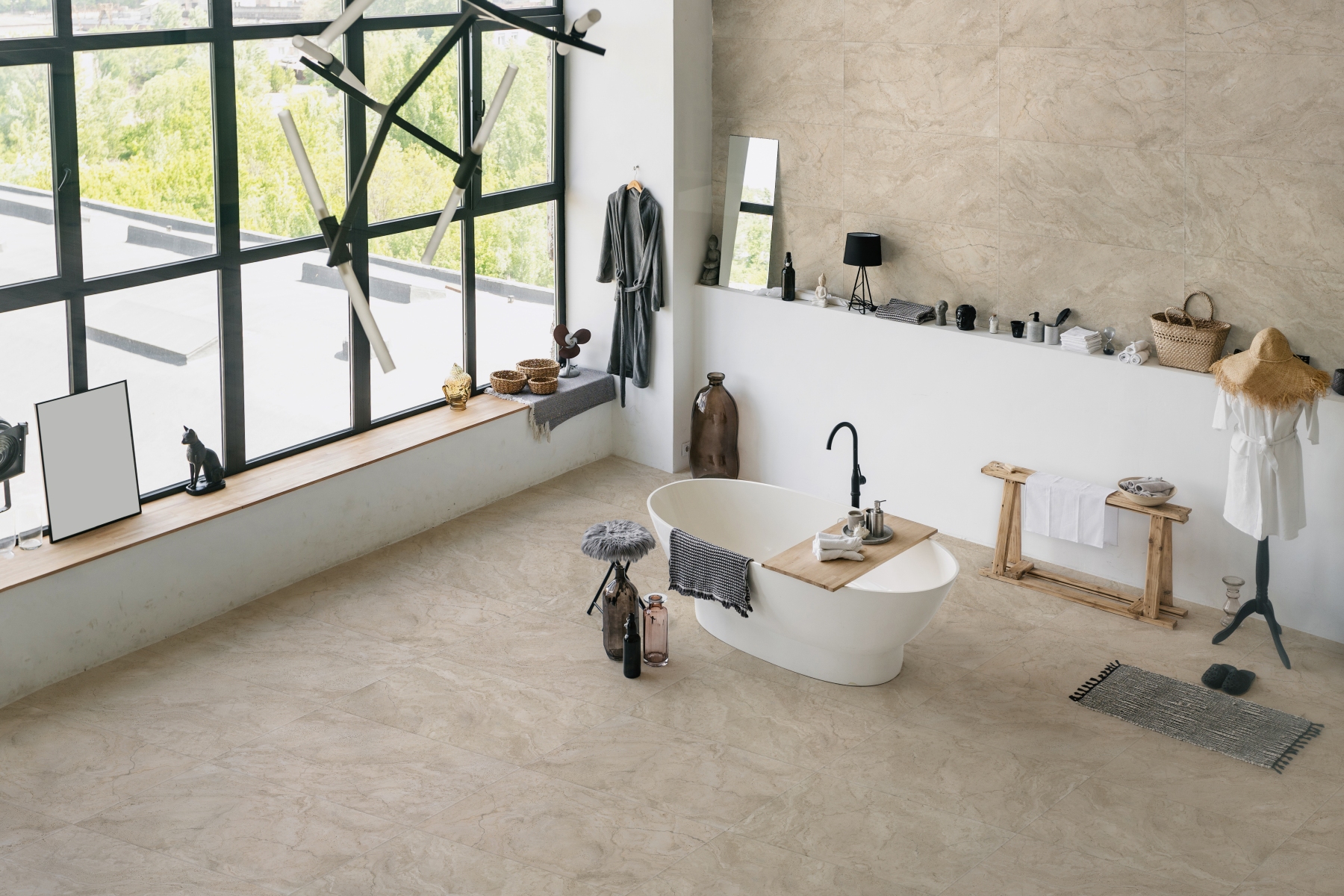 Kaasaegne valgusküllane vannituba suurte akendega, kus on keskne vabaduseisuga vann, hele beež kivimustriga põrand ja seinaplaadid. Riiulil on mitmesuguseid aksessuaare, rätikud ja kaunistused, aknalaual on dekoratiivkujud ning toas seisab ka mütsiga mannekeen.