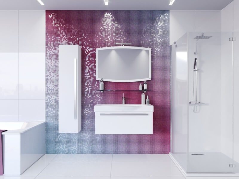 Modernne vannituba valge m&ouml;&ouml;bliga, mille taustaks on roosa-lilla l&auml;ikega mosaiiksein. Komplektis on k&otilde;rge seinakapp, valamukapp ja kergelt kaardus valgustatud peegel.