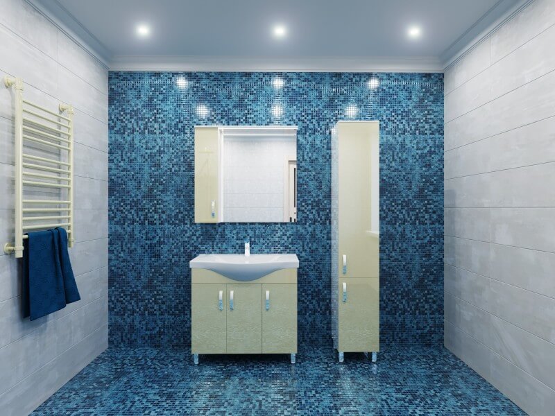 Hele l&auml;ikiv vannitoam&ouml;&ouml;bel sinise mosaiikplaadiga taustal. Komplekti kuuluvad valamukapp, k&otilde;rge kapp ja peegliga seinakapp.