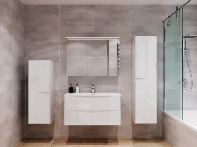 Valge l&auml;ikiv vannitoam&ouml;&ouml;bel modernsel hallil taustal. Komplekti kuuluvad valamukapp, kaks k&otilde;rget seinakappi ja kolmest osast peeglikapp valgustusega.