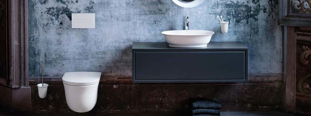 Tume eklektiline vannituba suure sinakashalli valamukapi, ümarvalamu ja valge seinapealse tualetipotiga. Taustal dekoratiivsed seinad.