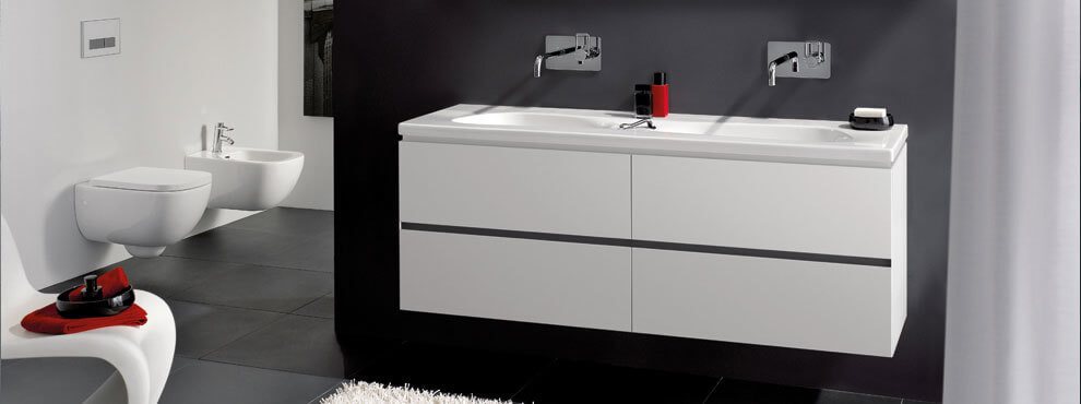 Modernne vannituba tumeda seina ja musta põrandaga. Seinapealne topeltvalamukapp kahe segistiga, seinale paigaldatud WC-pott ja bideekauss.