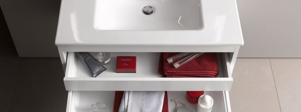 Valge vannitoakapp avatud sahtlitega, milles on punased ja valged rätikud, hambaharjad ning hooldustooted.