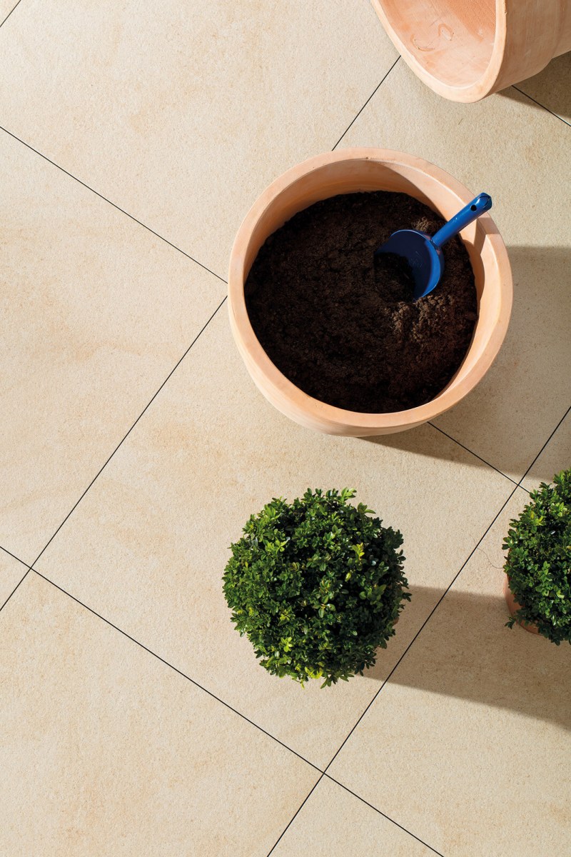 Heledates toonides kiviefektiga terrassiplaadid, millele on asetatud savipotid ja väikesed rohelised taimed – ideaalne valik avarale rõdule või aeda.