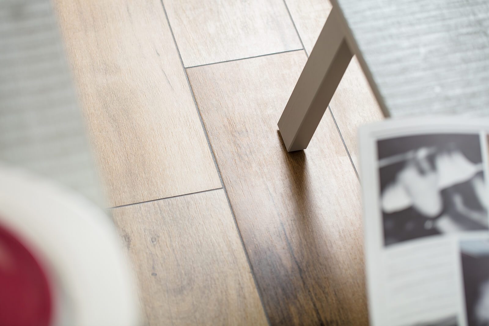 Heleda puidumustriga põrandaplaadid lähivaates, kõrval hall toolijalg ja udune ajakirjaleht.