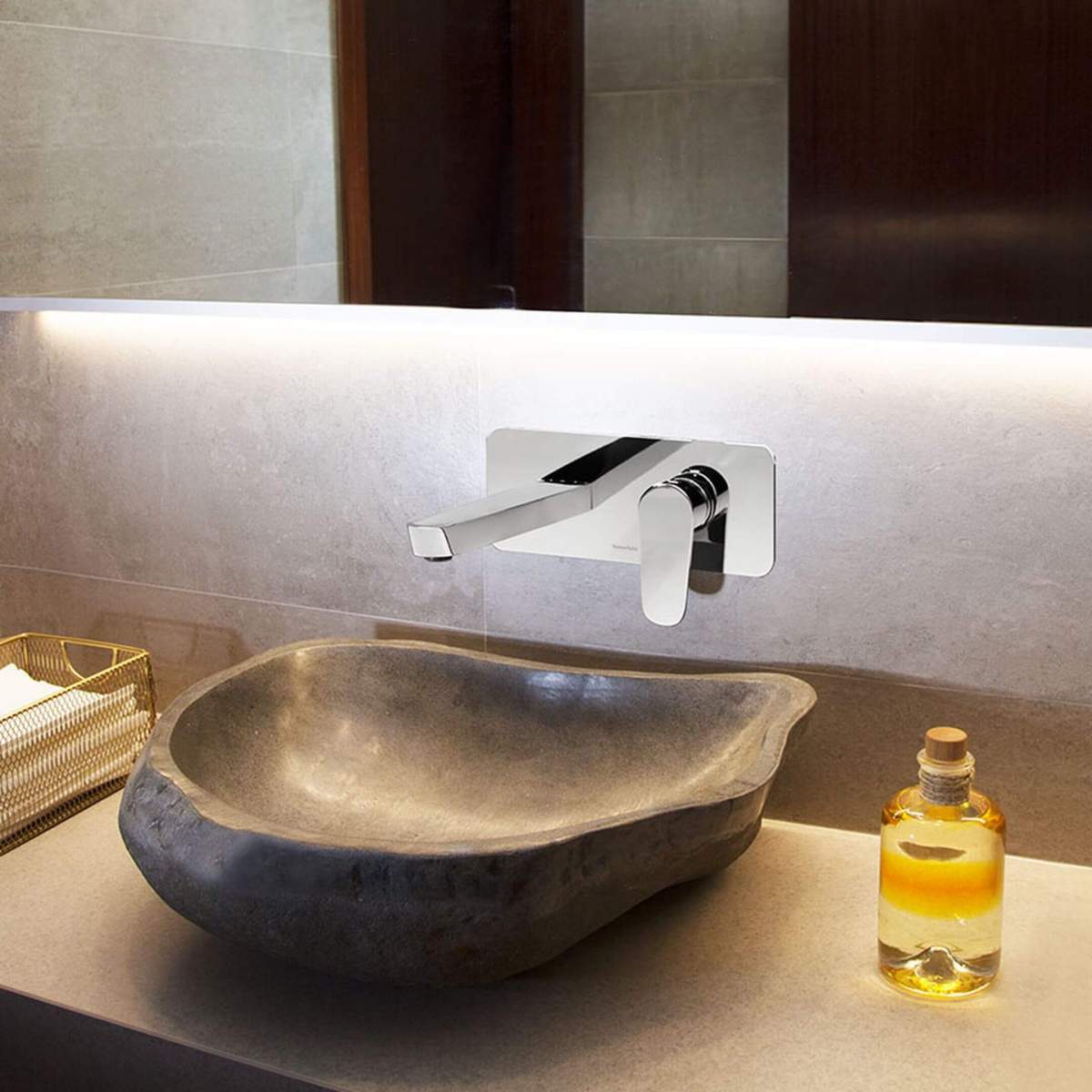 Seinale kinnitatud modernne segisti loodusliku kivivalamu k&otilde;rval, taustal sooja valgustusega peegel.