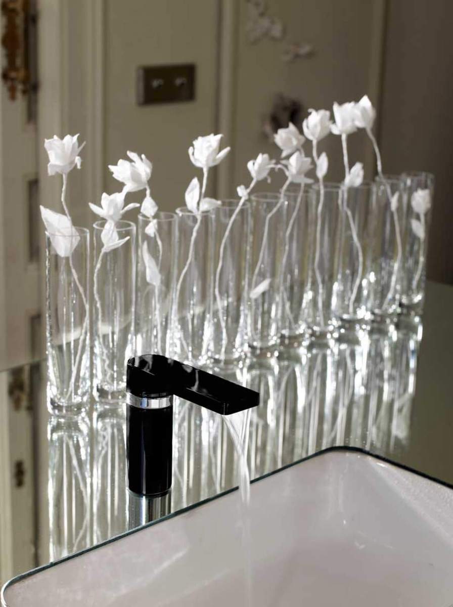 Must segisti valamu kohal, taustal reas l&auml;bipaistvad vaasid valgete kunstlilledega.