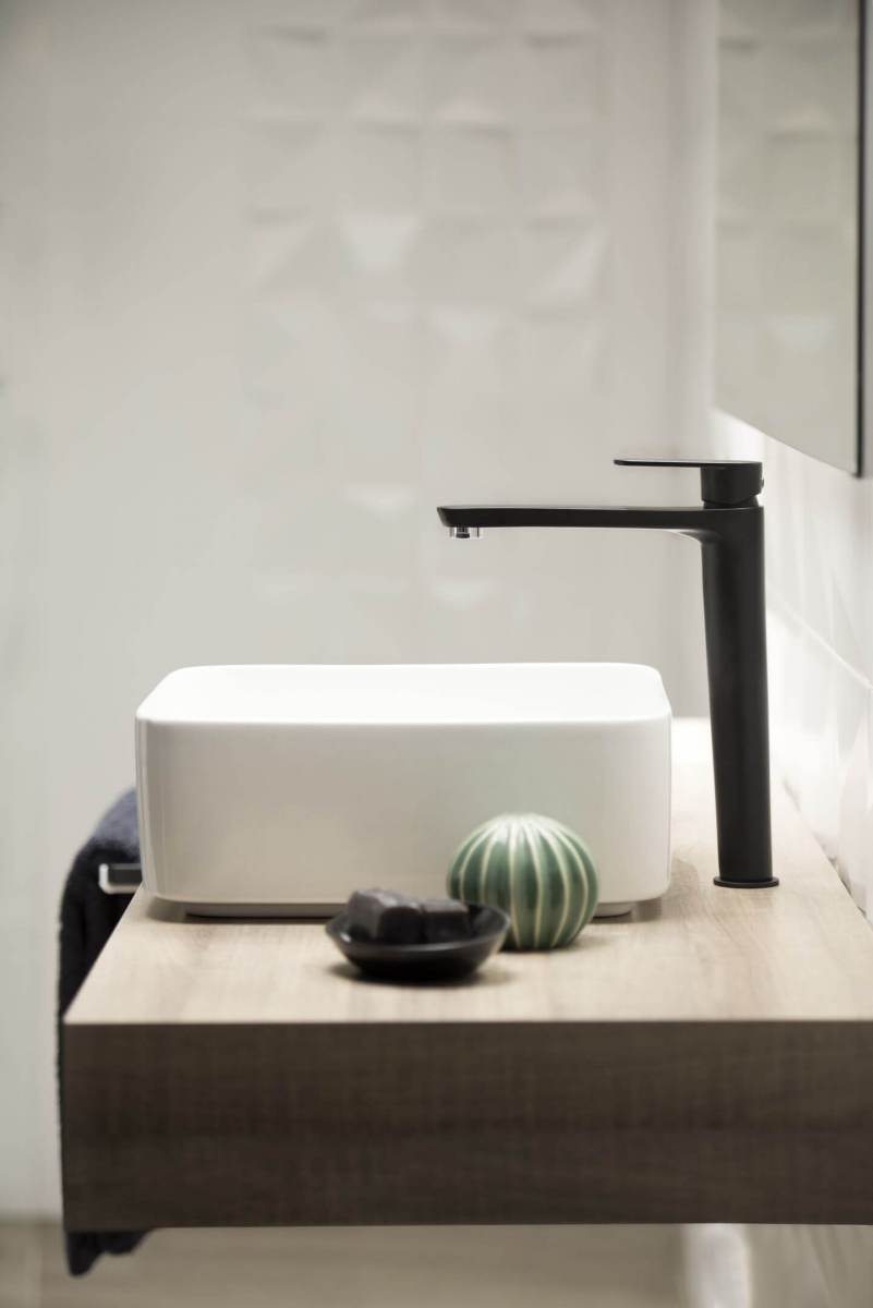 Must segisti valge kraanikausi k&otilde;rval, taustal peegel ja dekoratiivsed esemed puidust pinnal.