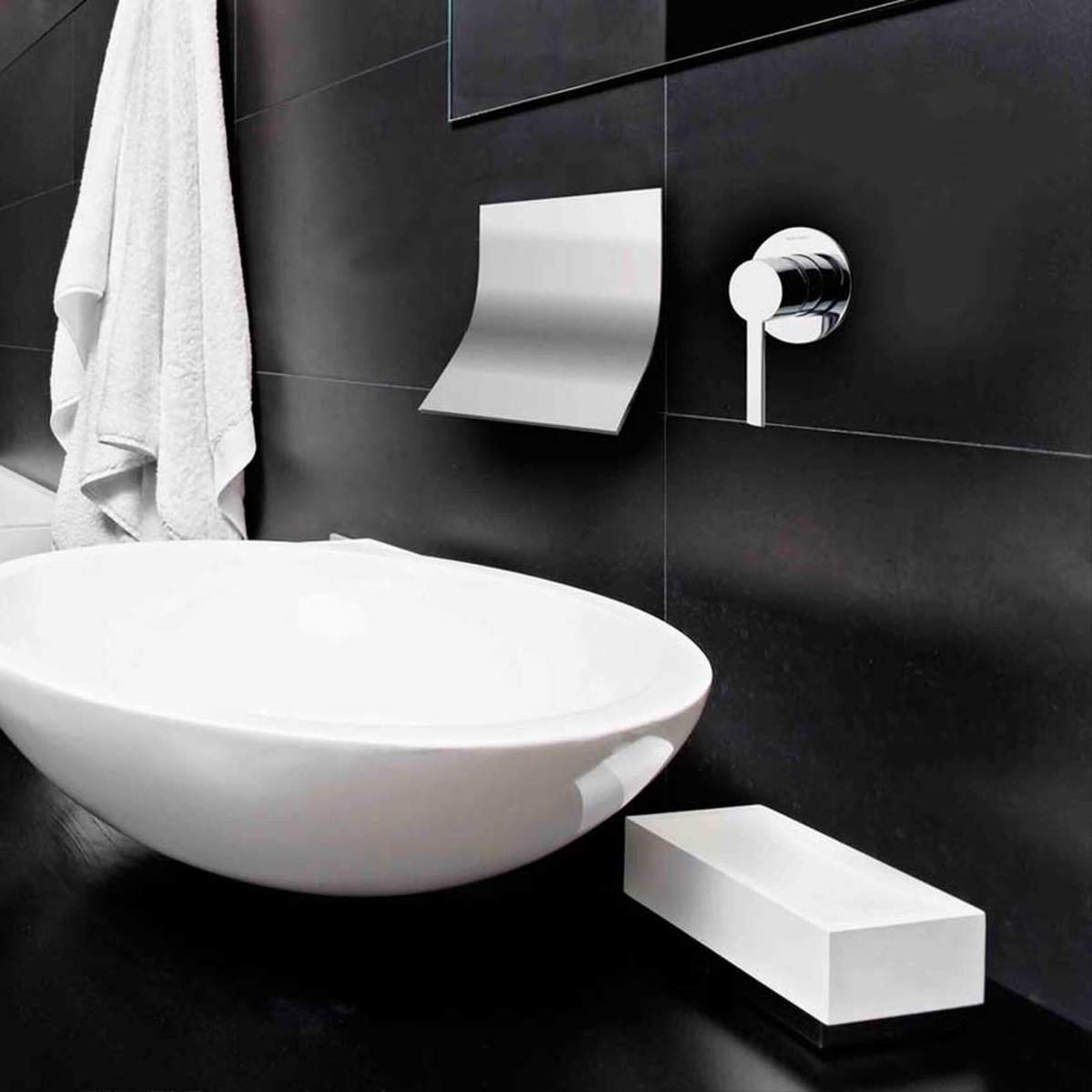 Musta tausta ees valge pesu&auml;mber ja modernne seinale kinnitatud segisti koos k&auml;ter&auml;tikuhoidiku ja valge disainielemendiga.