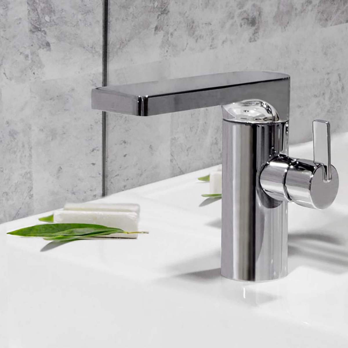 Silindrikujuline kroomitud segisti valge valamu ja kiviseinaga vannitoas.