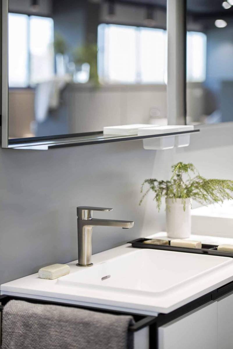 Kaasaegne segisti valgel kraanikausil, taustal peegel ja roheline taim vannitoas.