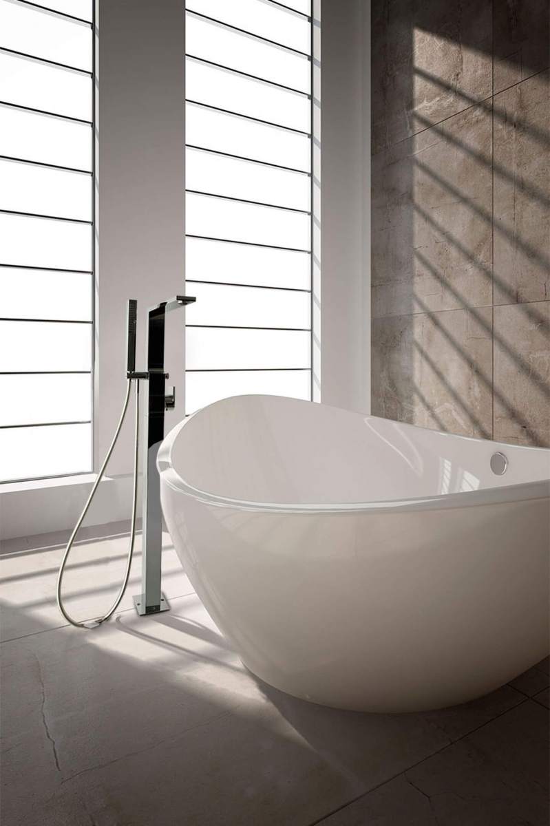 Vabalt seisev valge vann, mille k&otilde;rval on k&otilde;rge kraanikausisegisti ja du&scaron;ivoolik, suurte akende valgustatud vannitoas.