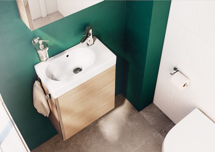 Kompaktne vannitoa kraanikauss rohelise seina ja puidust kapiga, kõrval WC-paberirull.