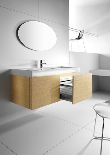 Valge kraanikauss puidust kapiga, mille sahtlid on avatud, ringikujuline peegel ja lihtne sisekujundus.