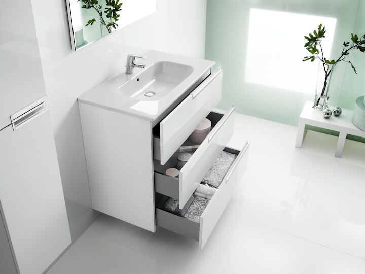 Valge kraanikauss kapp, mille sahtlid on avatud, taustal lihtne valge vannituba ja taimed.