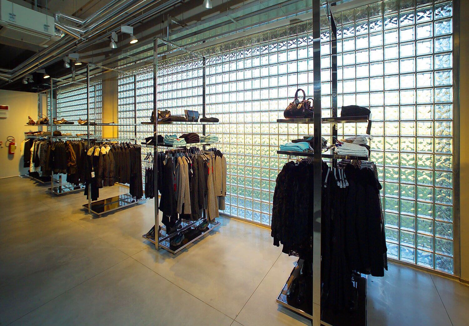 Rõivaste kaupluse sisustus klaasplokkide seina ees, kus on riidepuudel riideid ja kotte.