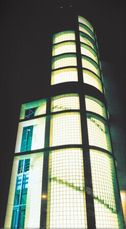 Klaasplokkidest seinaga kõrghoone öösel, valgustatud, sarnaneb kõrge torni kujuga.