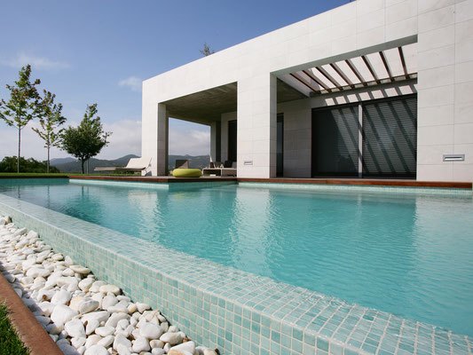 Kaunis bassein ja moodne maja, millel on valged plaadid ja roheline aiaruum.