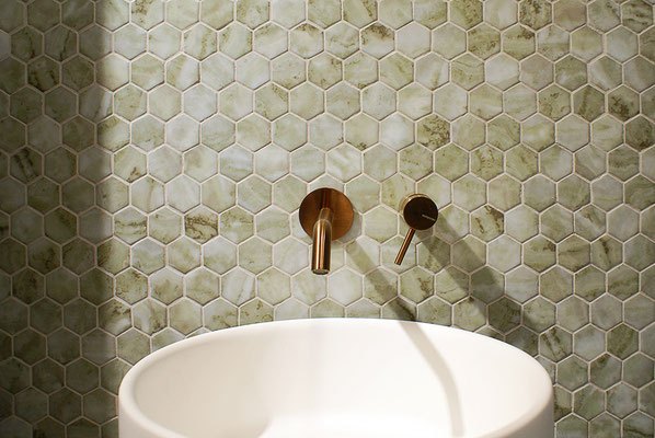 Valge valamu ja rohelise kuuekujulise plaatide seinaga vannituba.