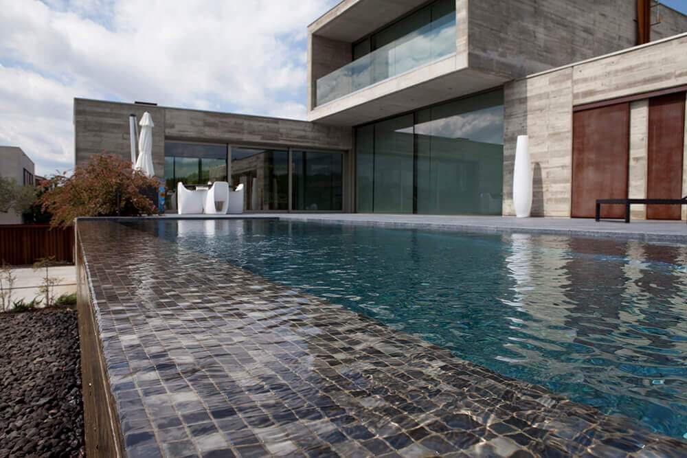 Kaasaegne villa &auml;&auml;retu basseiniga, mille serv ja sisevooder on kaetud tumeda klaasmosaiigiga. Bassein peegeldab taevast ja klaasfassaadi.