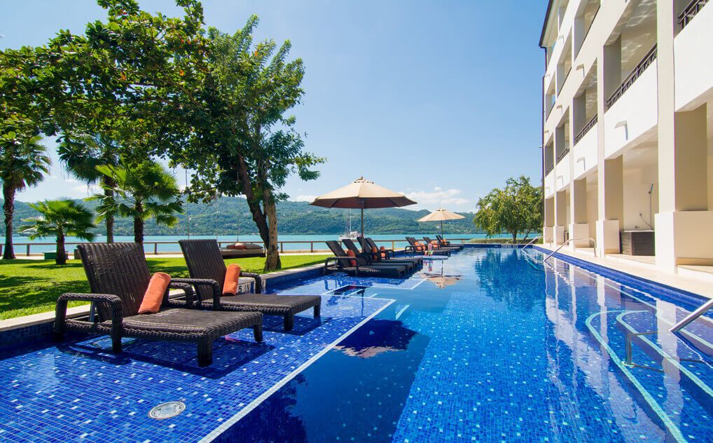 Sinise mosaiikplaadiga kaetud v&auml;libassein luksusliku hotelli juures, &uuml;mbritsetud lamamistoolide ja p&auml;ikesevarjudega. Taustal avanevad vaated j&auml;rvele ja rohelistele m&auml;gedele.