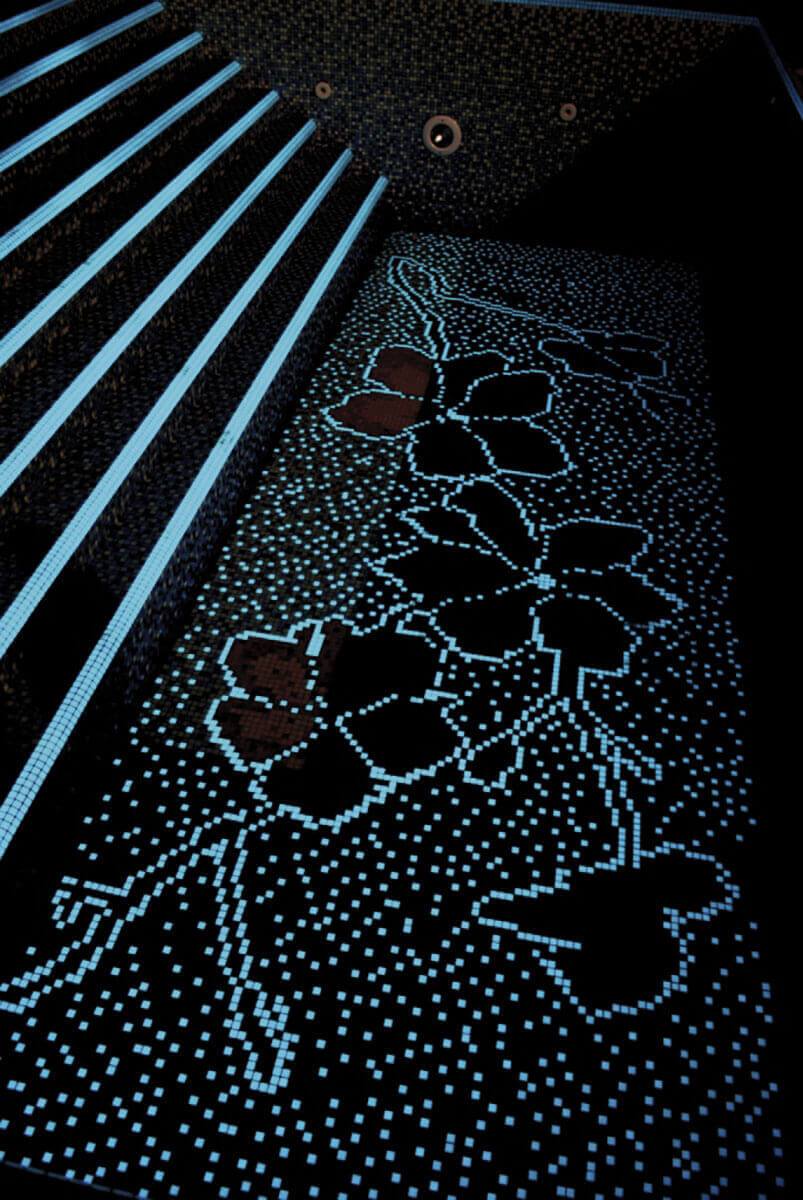 Tumedates toonides basseini sisepind, millele on ladutud kontrastne lillemuster v&auml;ikestest ruudukujulistest klaasmosaiikidest. Valgustus toob esile mustri kuju ja tekstuuri.