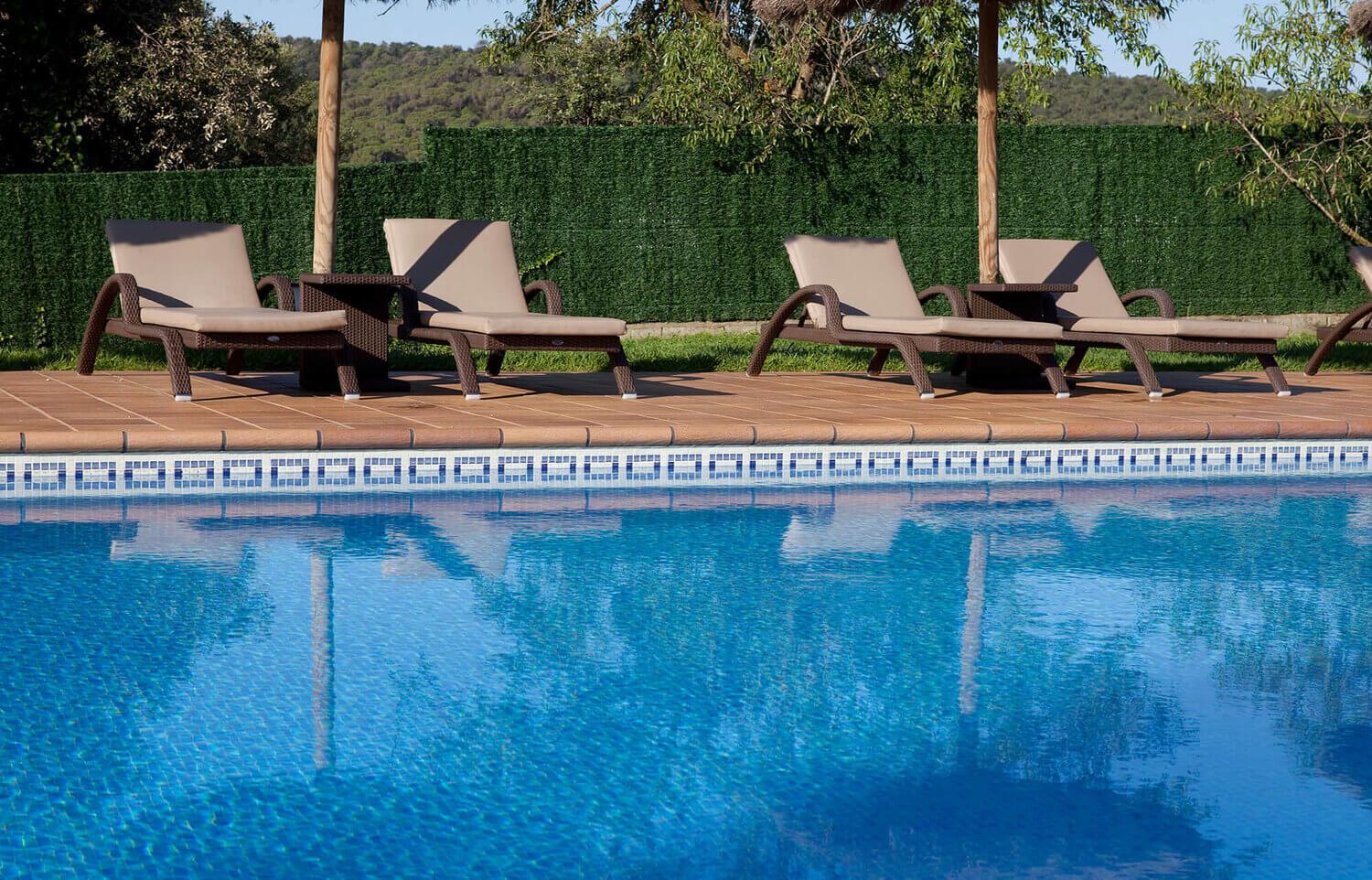 V&auml;libassein siniste mosaiikplaatidega, &auml;&auml;res pruunid lamamistoolid ja varjud, taustal rohelised puud ja hekk.